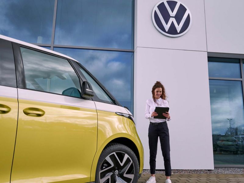 a VW expert standing outside a retailers holding an ipad next to a yellow ID.Buzz