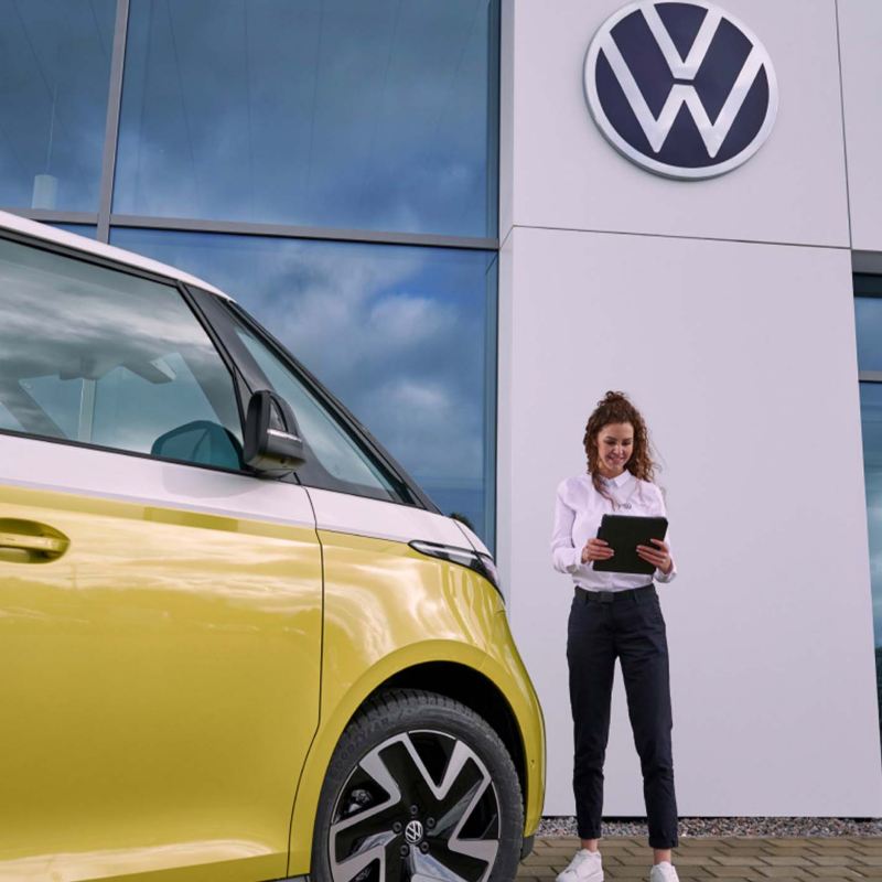 a VW expert standing outside a retailers holding an ipad next to a yellow ID.Buzz