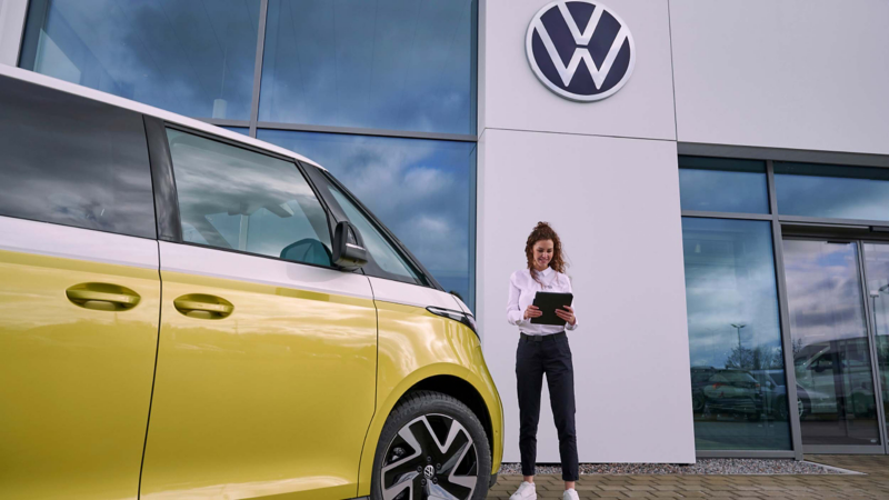 a VW expert standing outside a retailers holding an ipad next to a yellow ID.Buzz