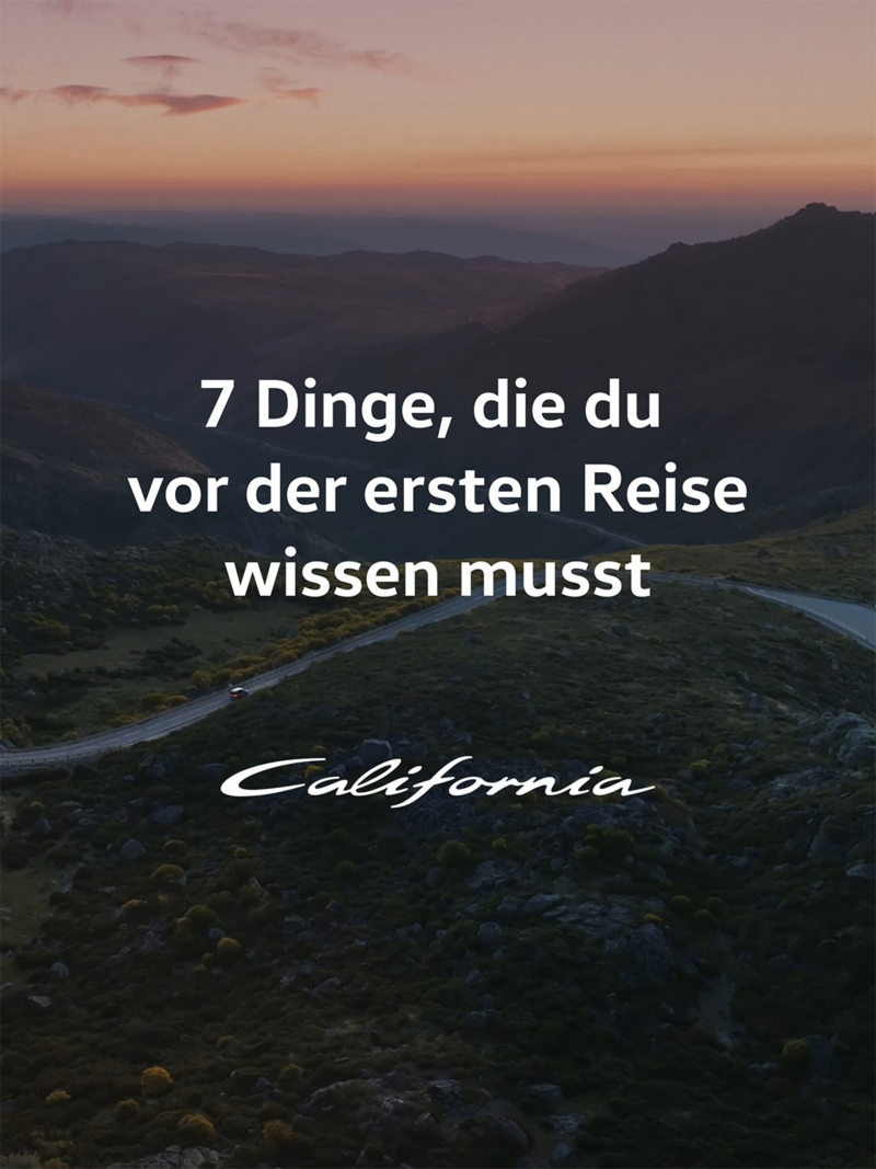 Ein VW California fährt gemächlich auf einer Straße durch eine malerische Berglandschaft.