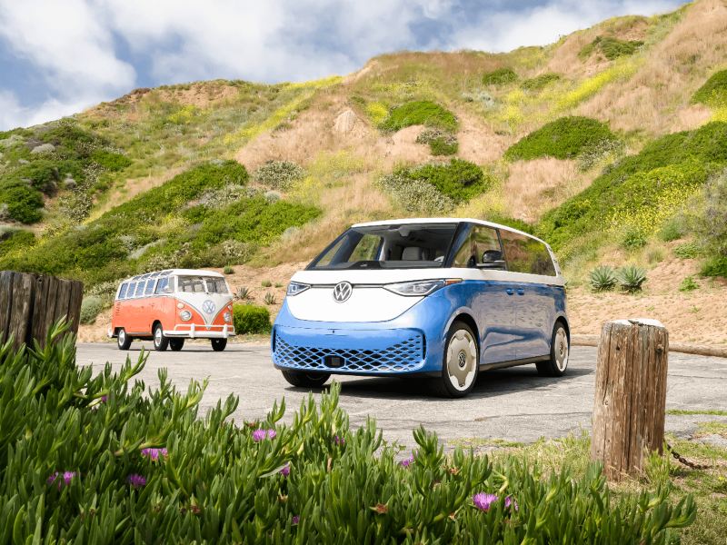 Un Volkswagen ID. Buzz 2025 bleu et blanc garé près d'une colline verdoyante.