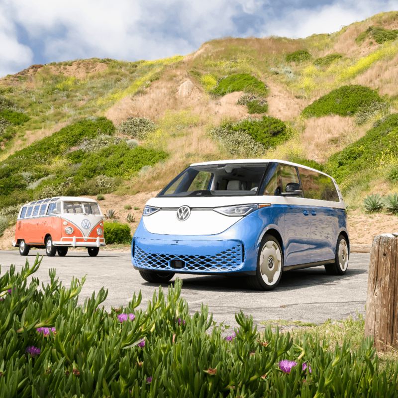 Un Volkswagen ID. Buzz 2025 bleu et blanc garé près d'une colline verdoyante.