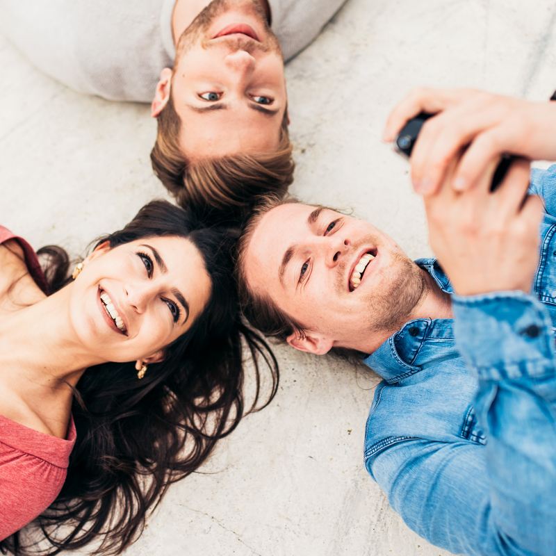 A woman and two men lying head to head looking at their smartphones