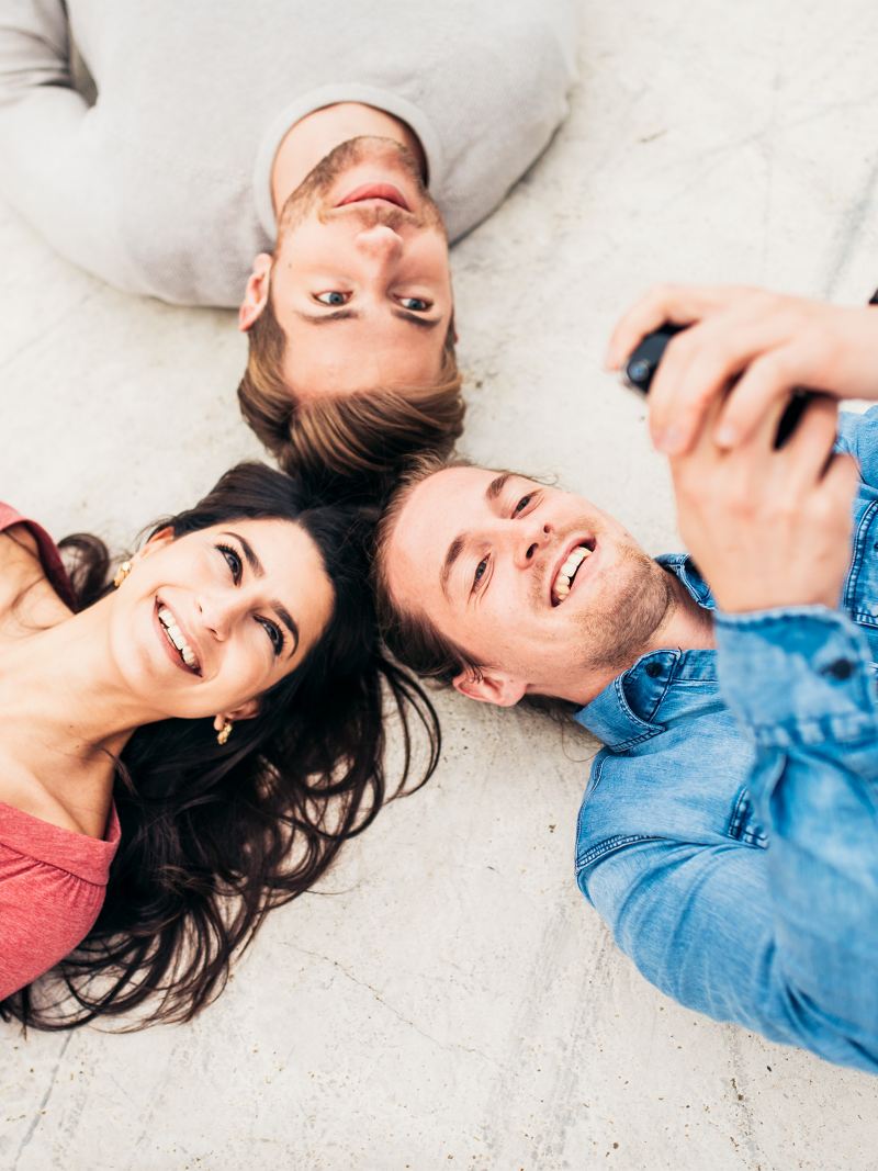 A woman and two men lying head to head looking at their smartphones