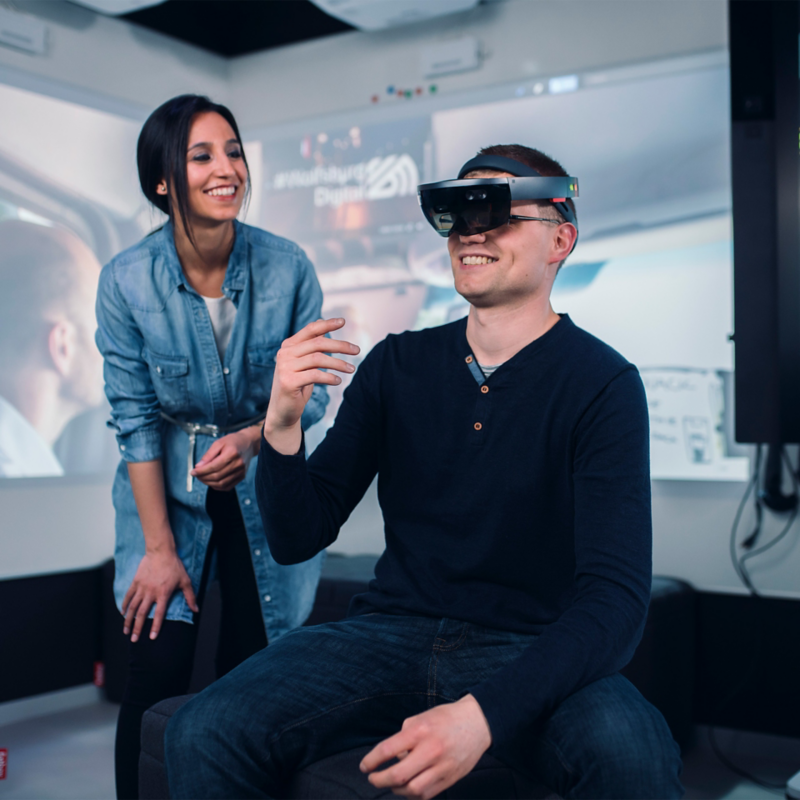 A young man wearing Volkswagen VR glasses and a young woman standing next to him