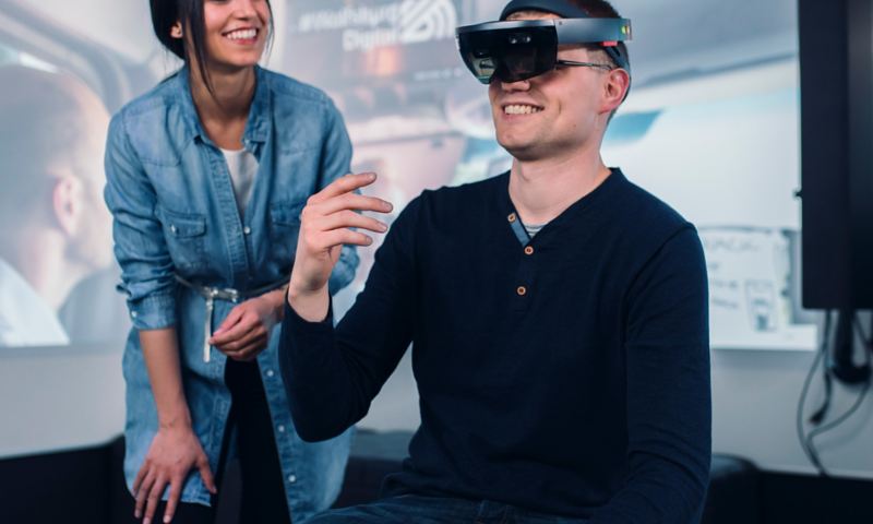 A young man wearing VR glasses and a young woman standing next to him
