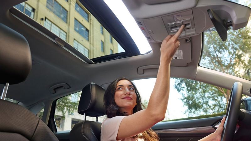 A woman inside the Volkswagen Jetta opening a sunroof.