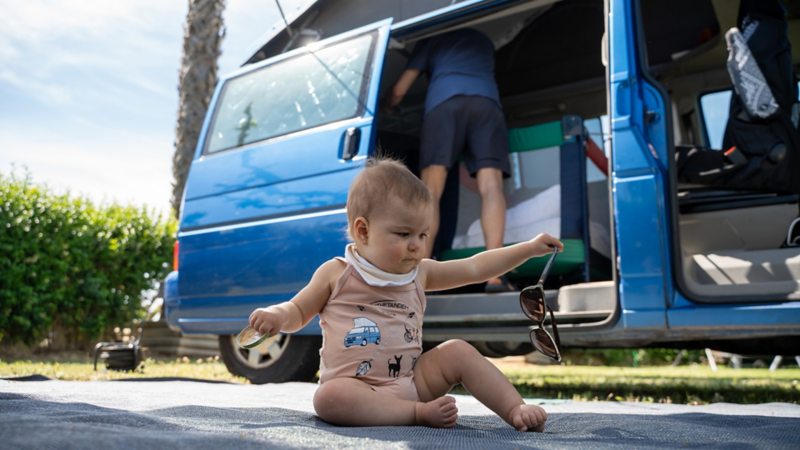 Un bebé sentado en el suelo delante de un VW Multivan.