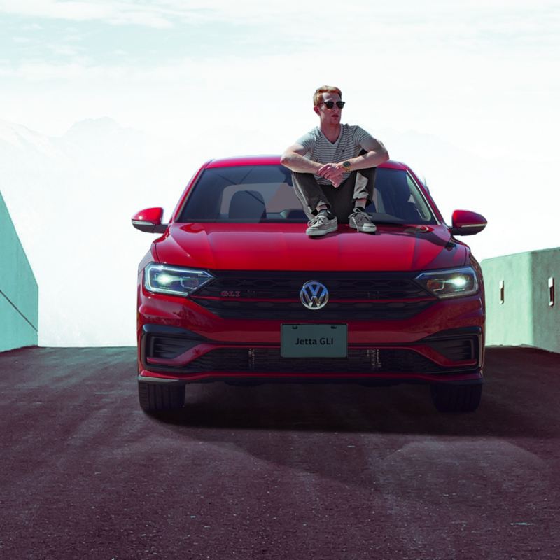 Hombre sentado sobre cofre de Jetta GLI, el carro deportivo de Volkswagen