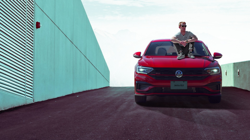 Hombre sentado sobre cofre de Jetta GLI, el carro deportivo de Volkswagen