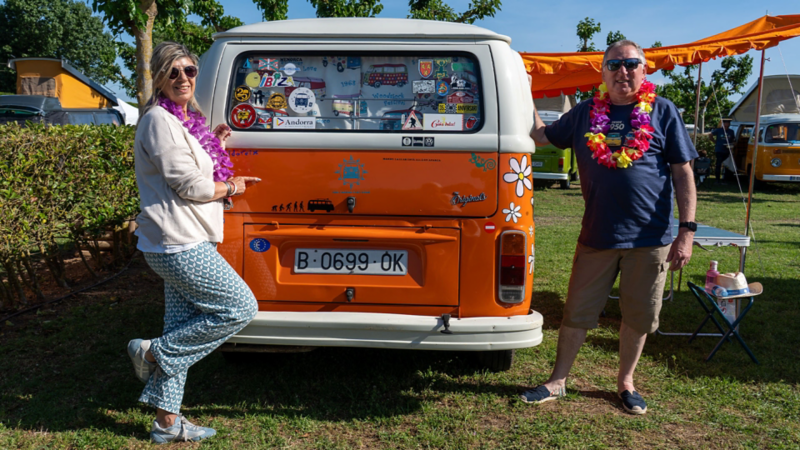 Una mujer y un hombre de pie junto a la parte trasera de una VW Clásica.