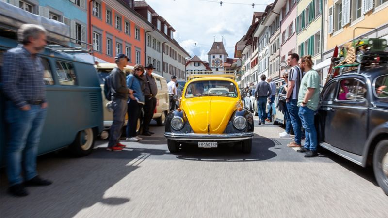 Ein schwarz-gelber VW Käfer fährt durch ein Dorf