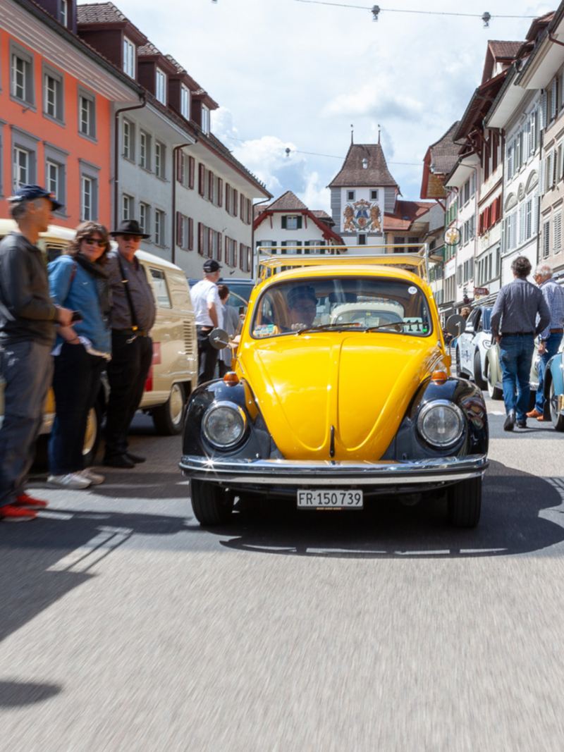 Un Maggiolino VW nero e giallo attraversa un villaggio