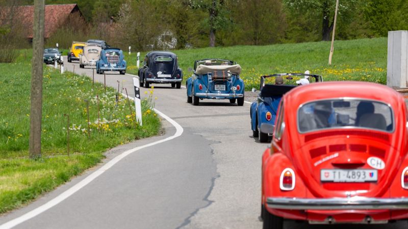 Plusieurs Coccinelles VW roulent sur une route de campagne