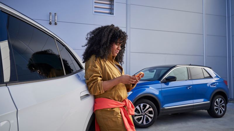 Kvinna lutad på en vit VW som tittar på sin mobil.