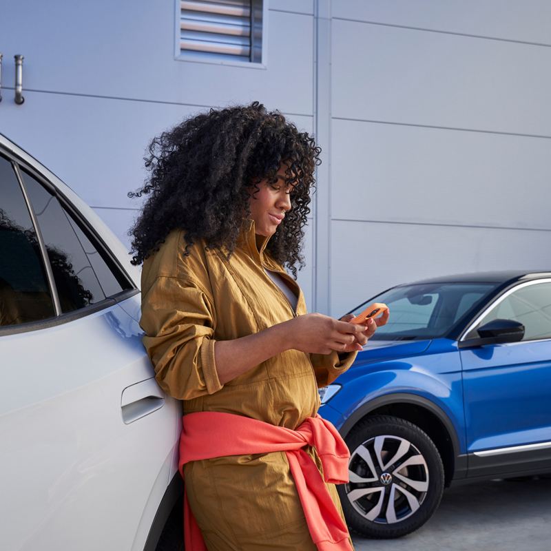 Naine toetub vastu Volkswagenit ja vaatab oma mobiiltelefoni