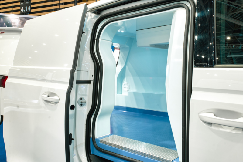 Porte latérale coulissante d'un ID. Buzz Cargo blanc ouverte, donnant sur un espace de chargement isotherme avec un marchepied en métal et un revêtement intérieur bleu.
