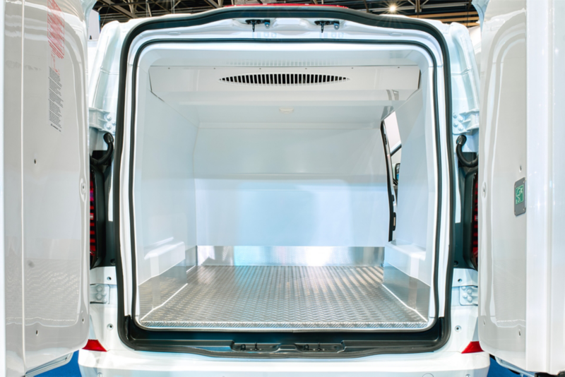 Vue de l'arrière d'un VW Transporter Frigorifique utilitaire blanc avec les portes ouvertes, dévoilant un espace de chargement vide doté d'un plancher en métal et de parois blanches.