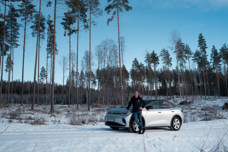 Person står framför en vit ID. 5 GTX i en skog med snö.