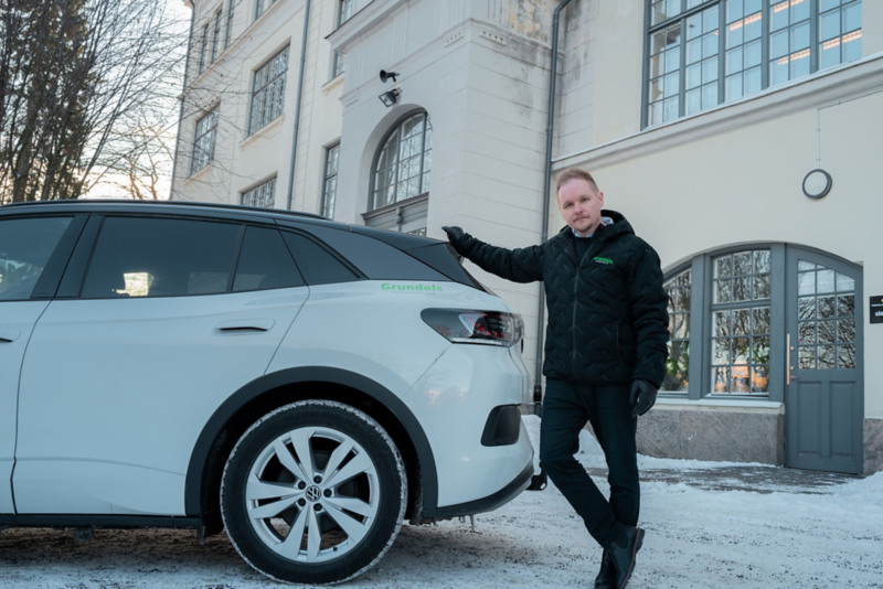 Daniel står bakom en vit Volkswagen ID.4 sedd från sidan med en byggnad i bakgrunden