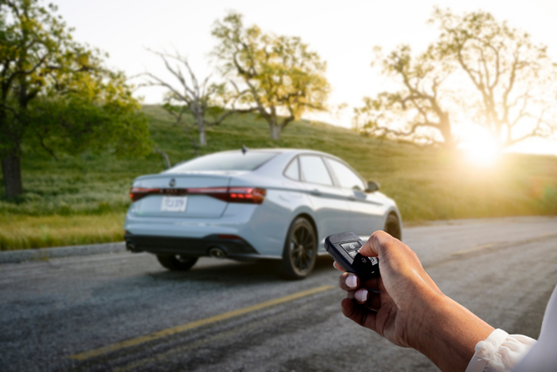 Rear angle of a Jetta GLI shown in Monument Gray parked with wooded hills in the background.  