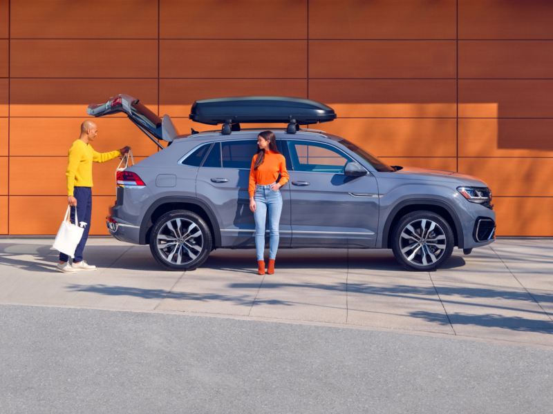 A young woman leaning on the Volkswagen Taos while a man is packing bags in the trunk. link out to VW “accessories” page