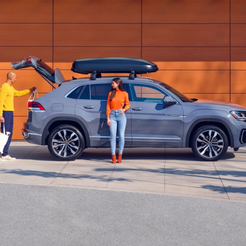 A young woman leaning on the Volkswagen Taos while a man is packing bags in the trunk. link out to VW “accessories” page