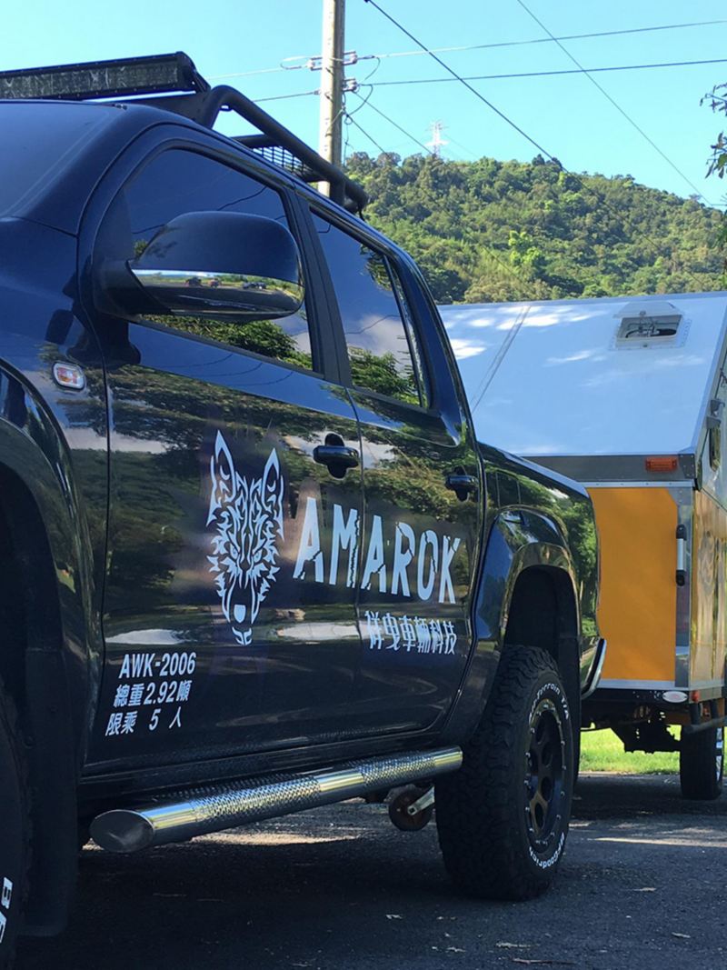 黑色Amarok拖著越野型露營拖車，停在山邊小路上