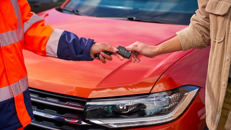 VW service employee hands car key to customer, a VW car in the background