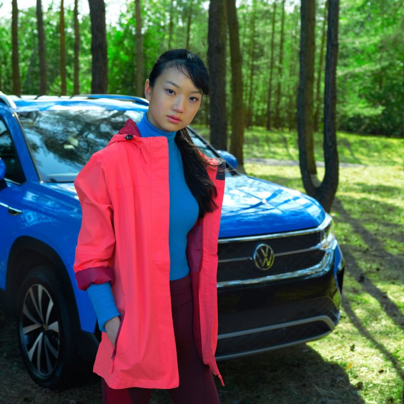 Une fille en veste corail près de la Volkswagen bleue dans une forêt