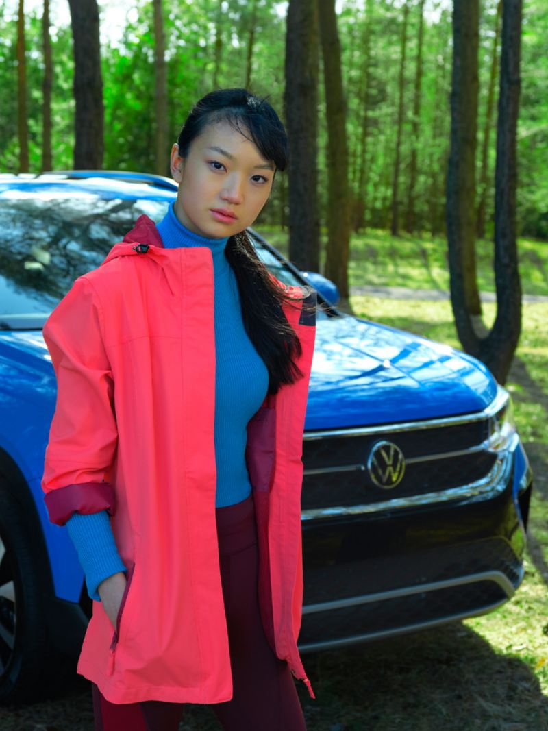 Une fille en veste corail près de la Volkswagen bleue dans une forêt