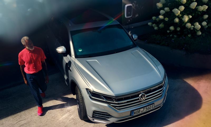 Volkswagen Touareg eHybrid couleur argent, vue de face, dans une allée, un homme passant devant