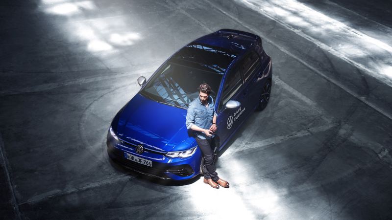 Ein Mann lehnt an seinem blauen VW Golf R