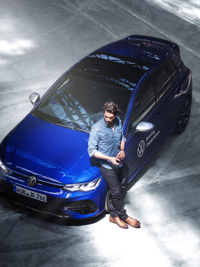 A man leaning on his blue VW Golf R
