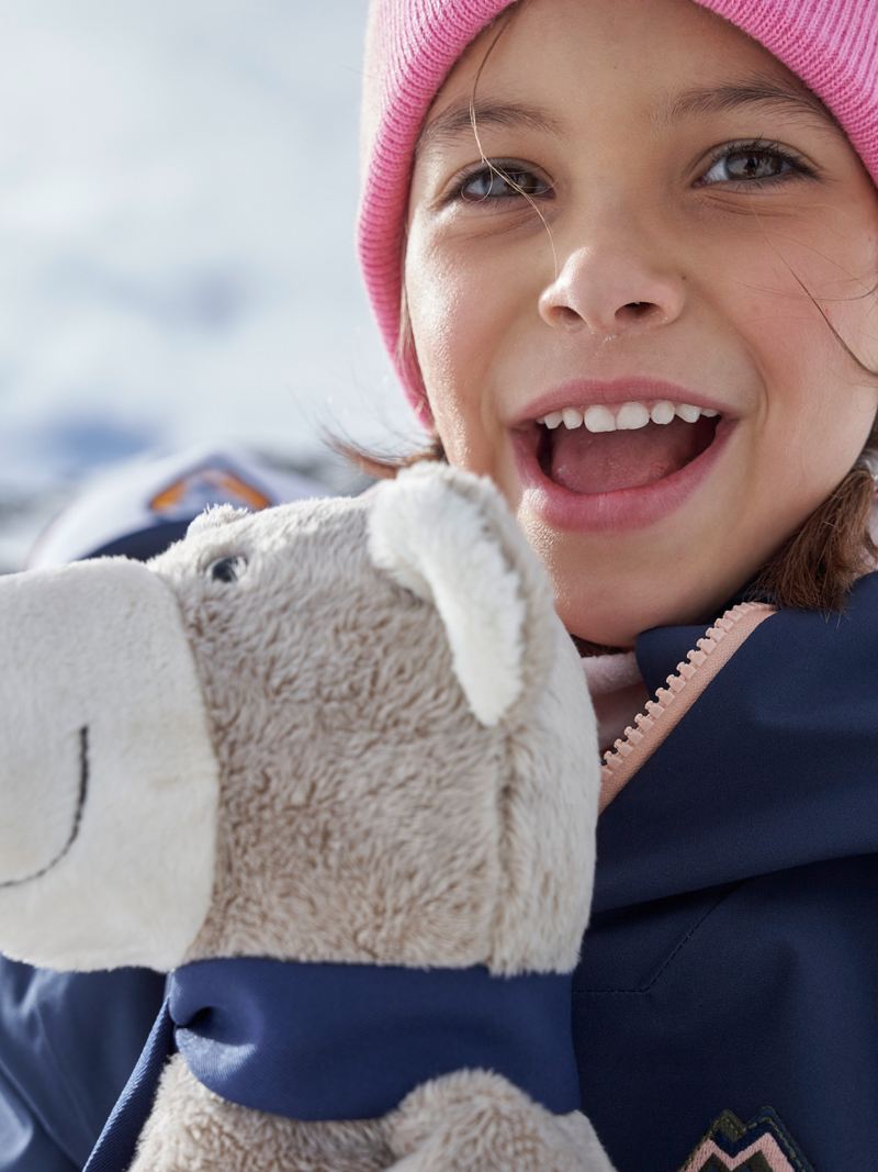 Ein Mädchen mit ihrem Kuschelbär von VW Zubehör genießt die Zeit im Schnee