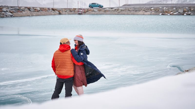 Ein Pärchen steht an einem zugefrorenen See und schaut sich verliebt an