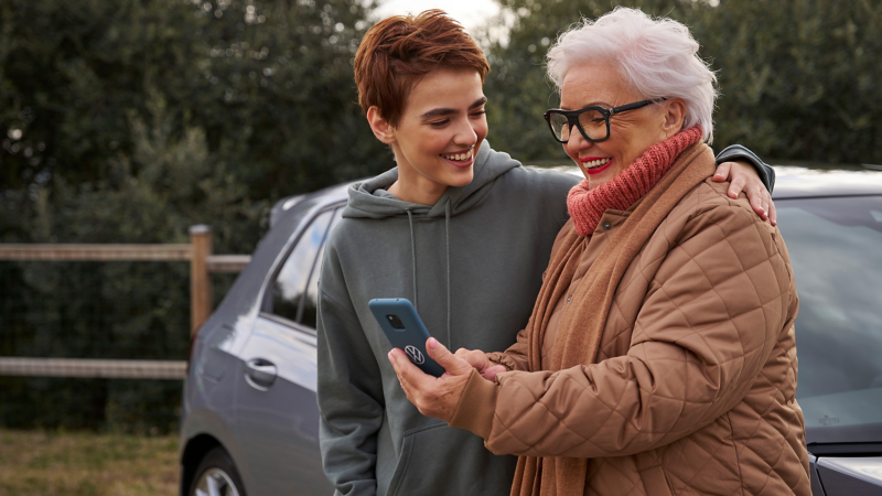 Two women in front of a VW car looking at a smartphone