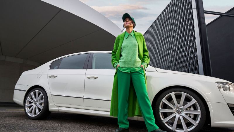 Eine Frau in grüner Kleidung steht nach dem Werkstatttermin beim VW Economy Service vor ihrem Passat B6