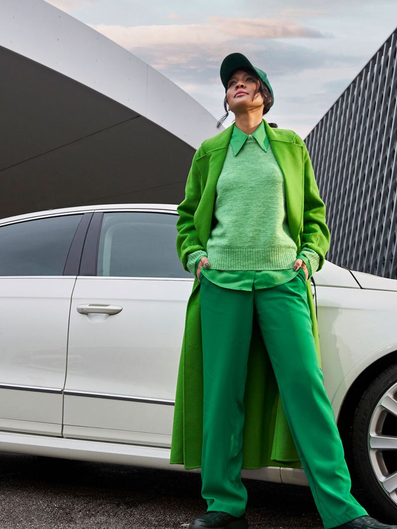 Eine Frau in grüner Kleidung steht nach dem Werkstatttermin beim VW Economy Service vor ihrem Passat B6