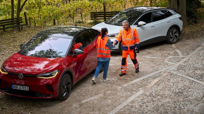 Woman with safety vest and Volkswagen Roadside Assistance employee next to two VW ID. cars