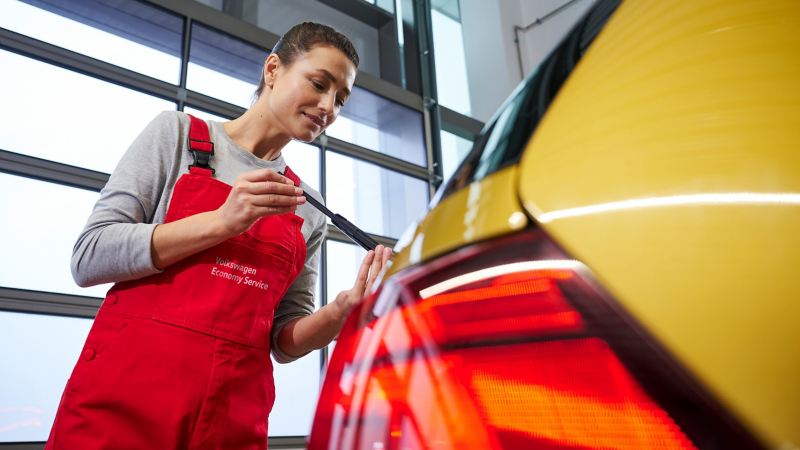 Eine Servicemitarbeiterin überprüft einen Volkswagen in der Werkstatt – VW Economy Service