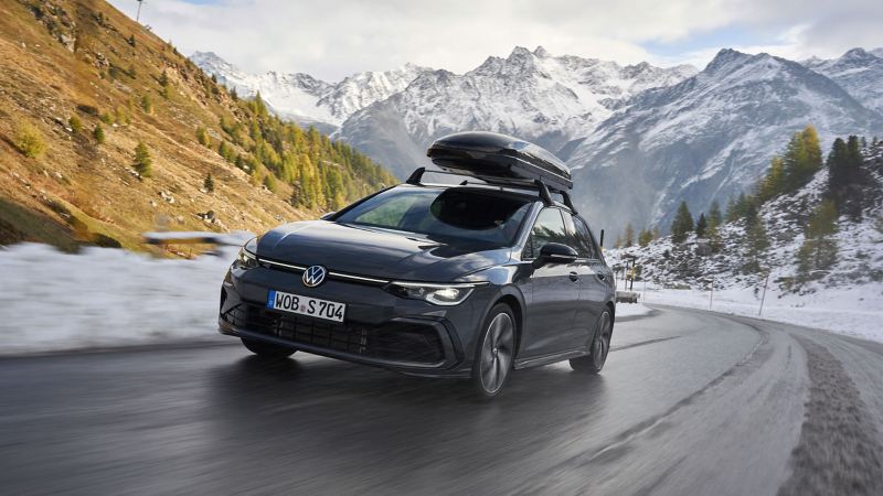 A VW Golf R-Line with complete all-season wheels drives through a snowy mountain landscape