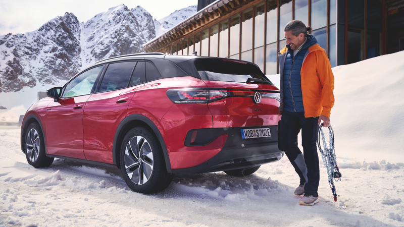 VW ID.4 GTX im Schnee vor einem Haus, am Heck steht Mann mit Schneekette in der Hand