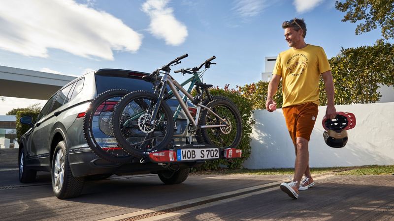 Man with bike helmets walking past a VW Tiguan Allspace with bicycle carrier at the rear