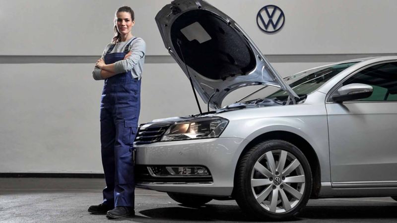 Campo totale di un meccanico Volkswagen appoggiato ad un veicolo il cui tetto del cofano anteriore è aperto.