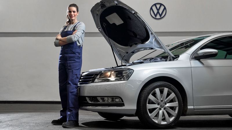 A VW service employee next to a Volkswagen with an open bonnet