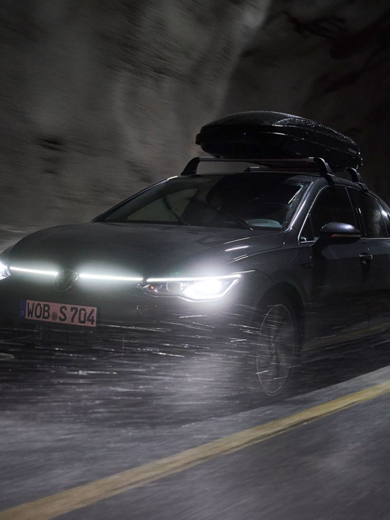 Un véhicule VW avec un coffre de toit passe dans un tunnel avec les phares allumés