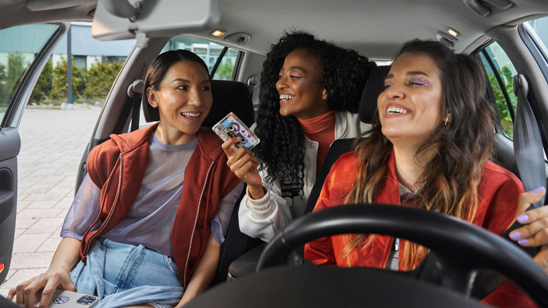 Woman in the driver's seat of a VW car shows her two friends a mixtape