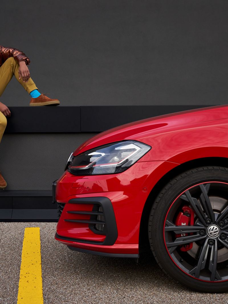 Ein glücklicher Mann neben seinem roten Golf 7 von Volkswagen