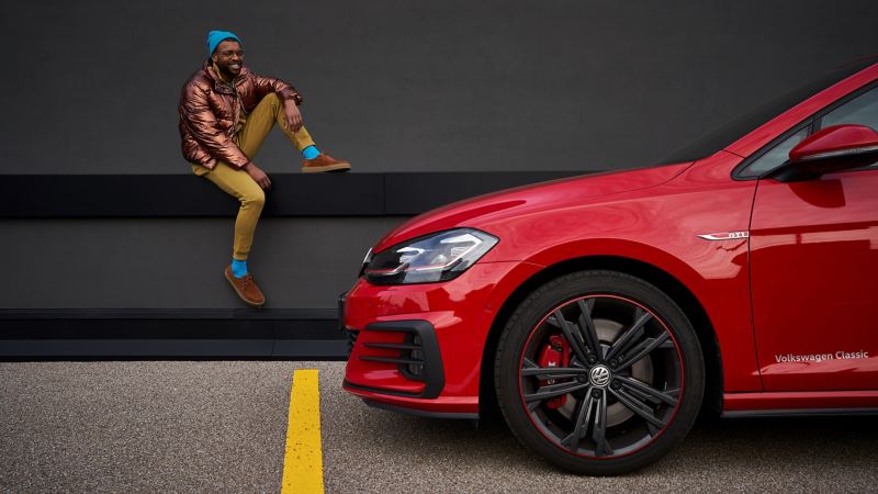 Un homme heureux à côté de sa Volkswagen Golf 7 rouge